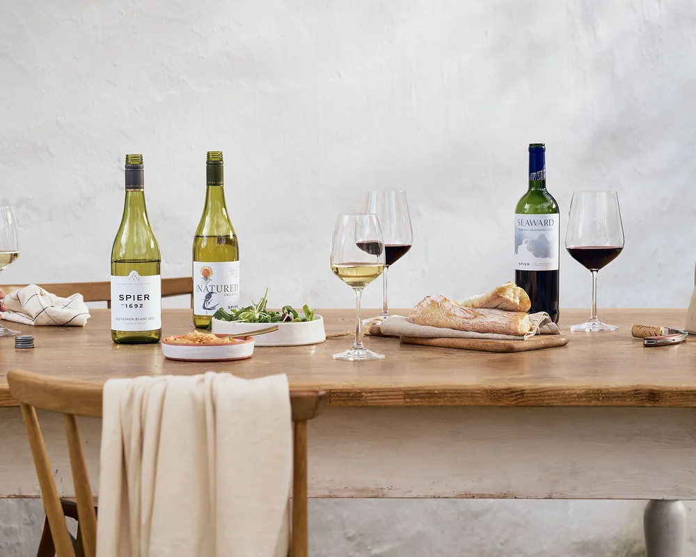 Spier Signature, Good Natured and Seaward wines on a farm table with bread, salad and glasses